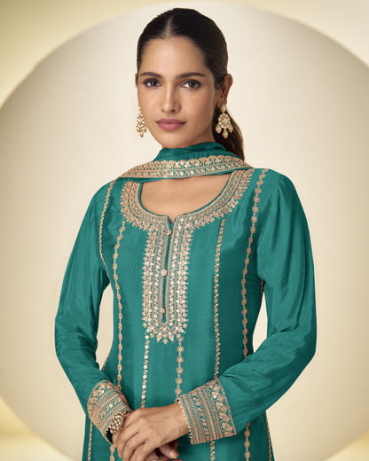 Woman wearing a teal embroidered traditional outfit on a beige background