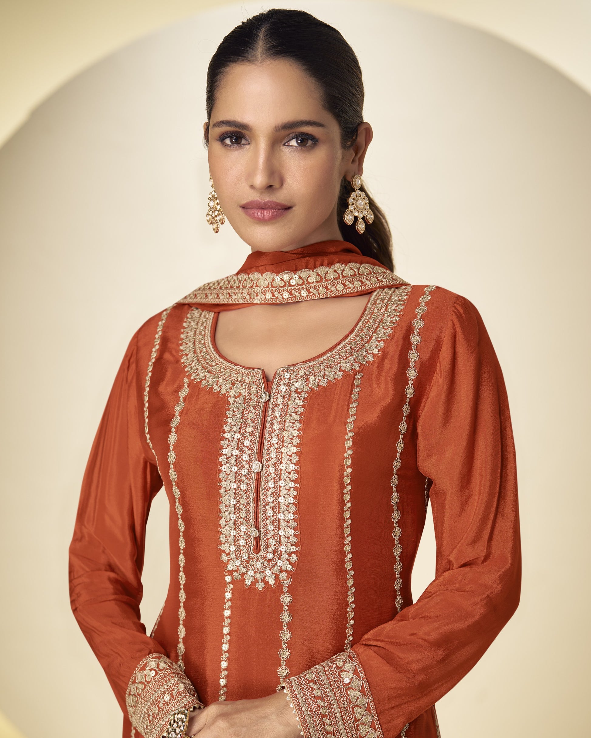 Woman wearing an orange embroidered traditional outfit on a beige background