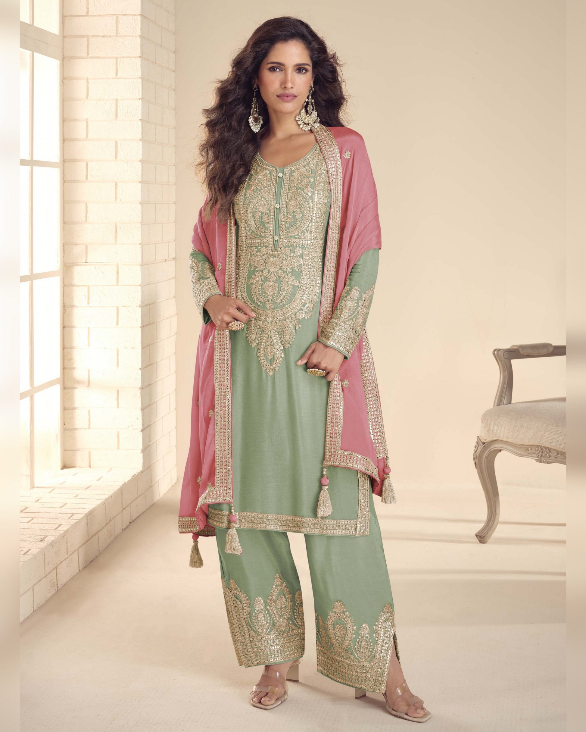 Woman wearing a traditional outfit with pink dupatta and green pants in a well-lit room.