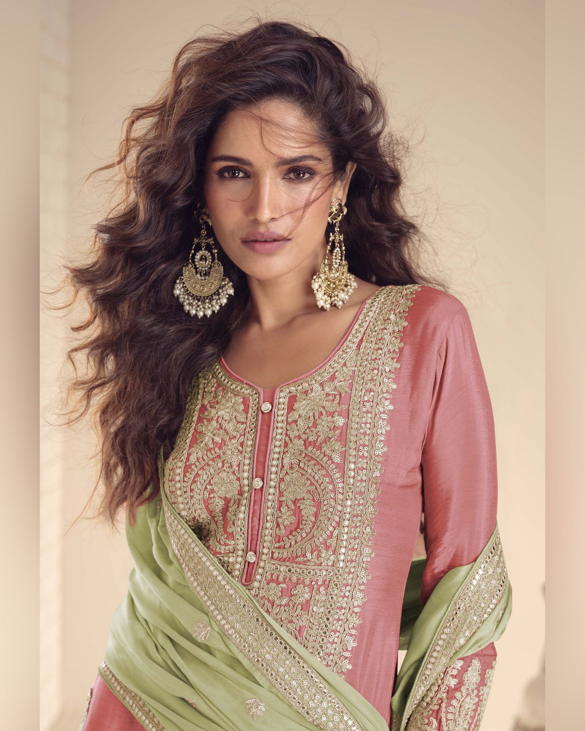 Woman wearing traditional embroidered pink and green outfit with jewelry against a neutral background