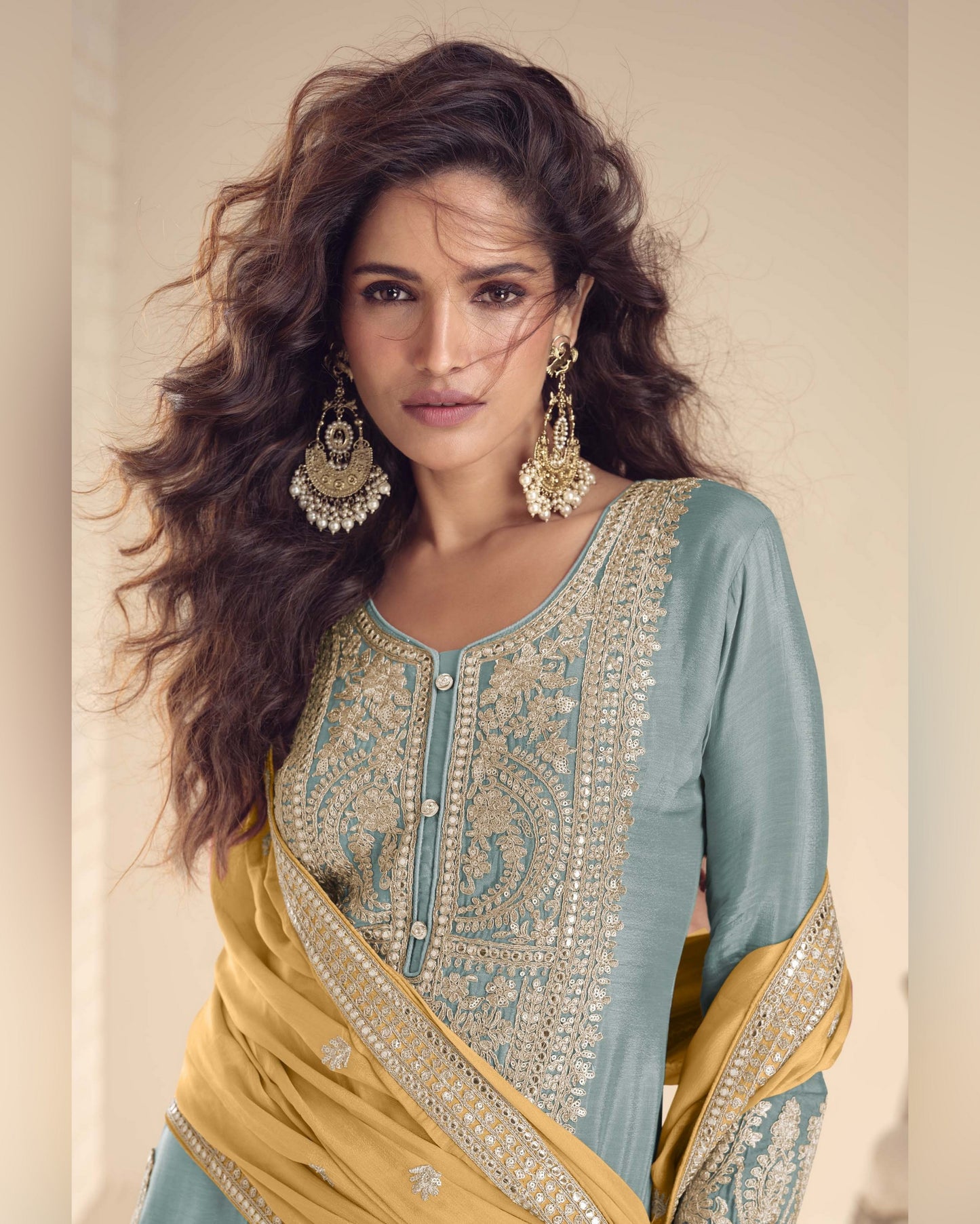 Woman wearing a traditional outfit with intricate patterns and jewelry against a neutral background