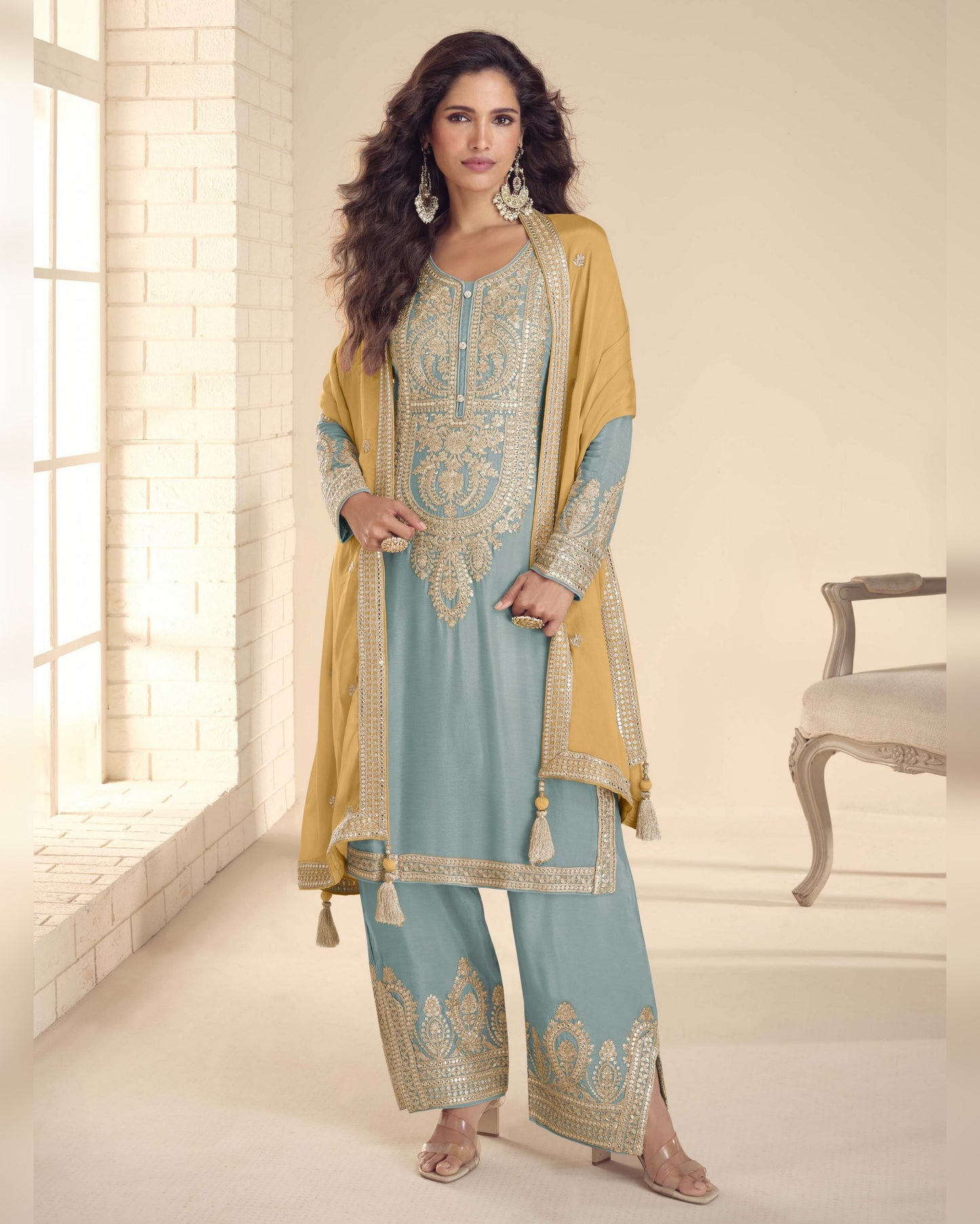 Woman wearing a traditional outfit with a light blue and yellow design in a bright room.