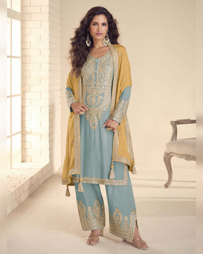 Woman wearing a traditional outfit with a light blue and yellow design in a bright room.