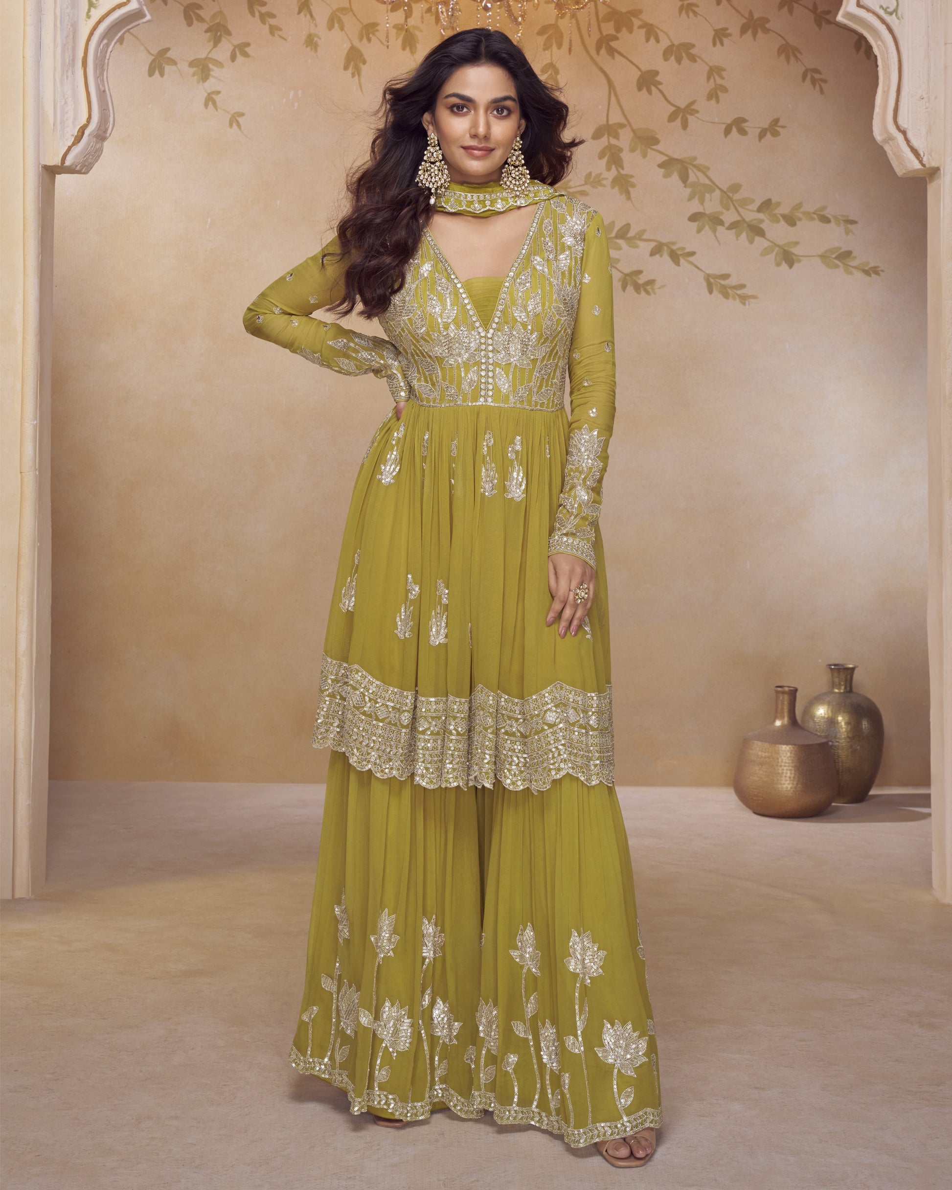 Woman wearing a green embroidered traditional outfit in a decorated room.