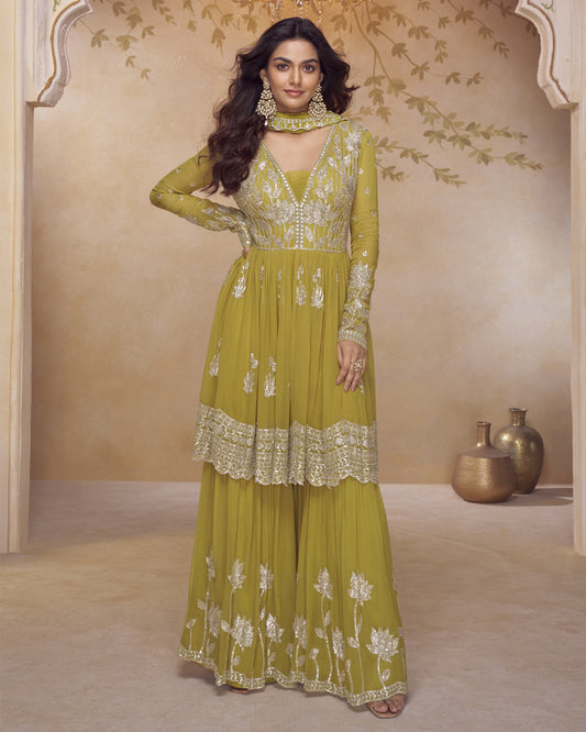 Woman wearing a green embroidered traditional outfit in a decorated room.