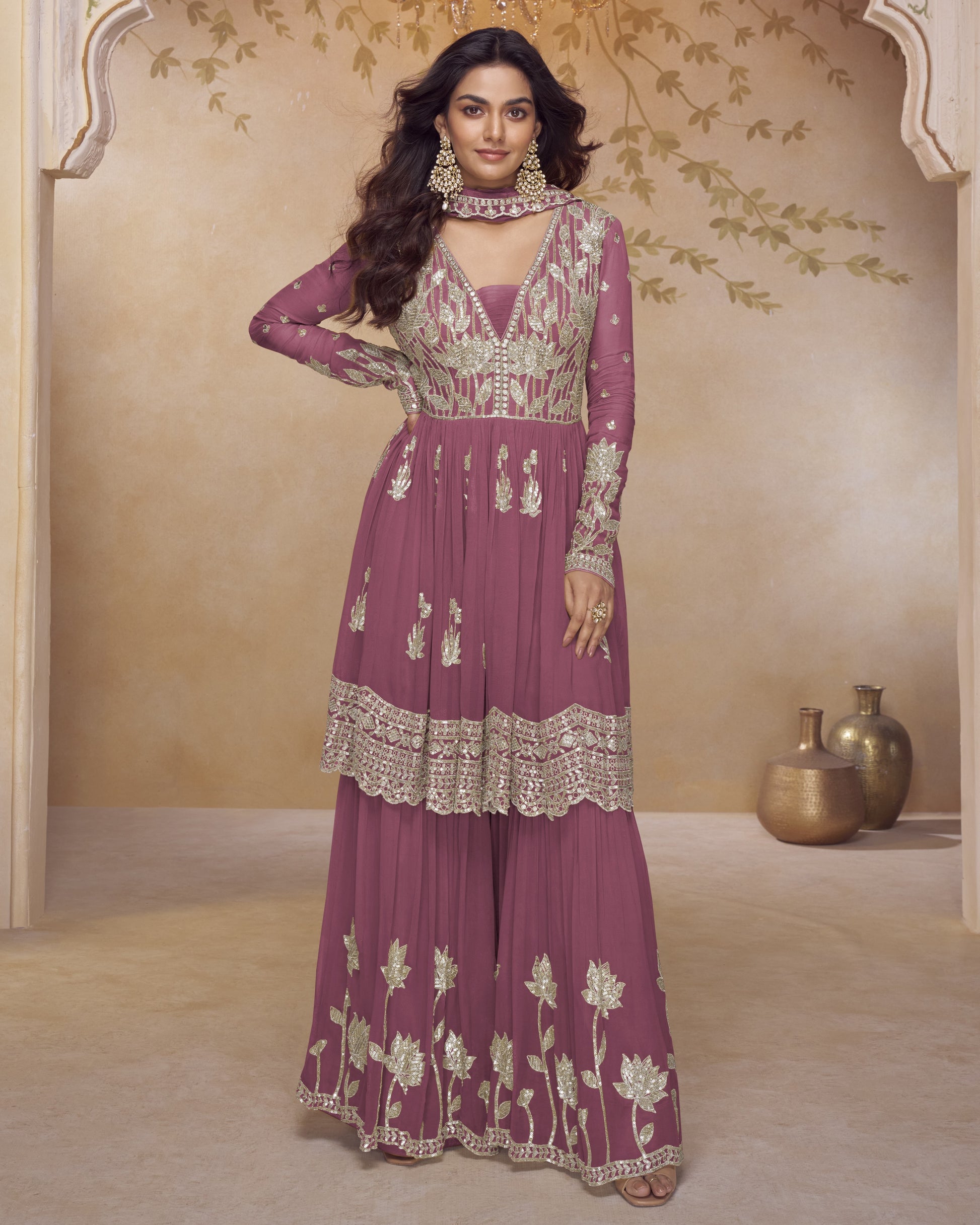 Woman wearing a purple embroidered traditional outfit in a decorated room.