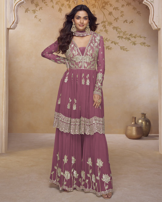 Woman wearing a purple embroidered traditional outfit in a decorated room.