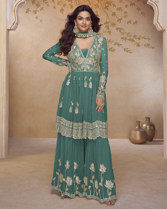 Woman wearing a green embroidered traditional outfit in a decorated room.
