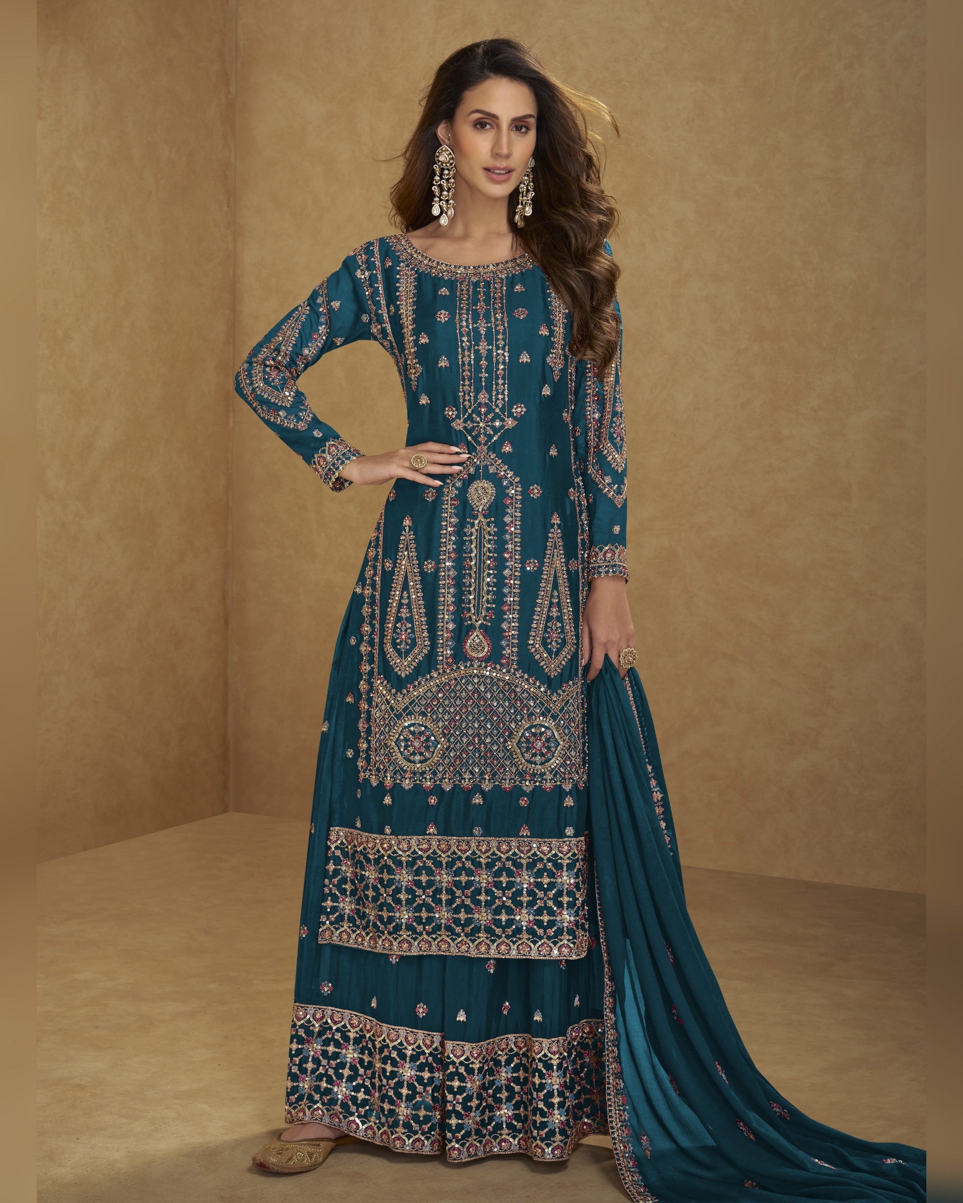 Woman wearing a teal embroidered traditional outfit with a beige background