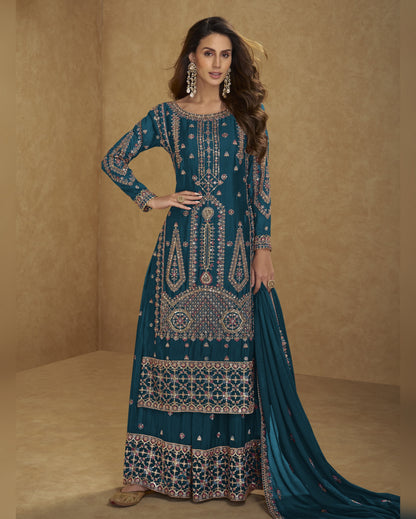 Woman wearing a teal embroidered traditional outfit with a beige background