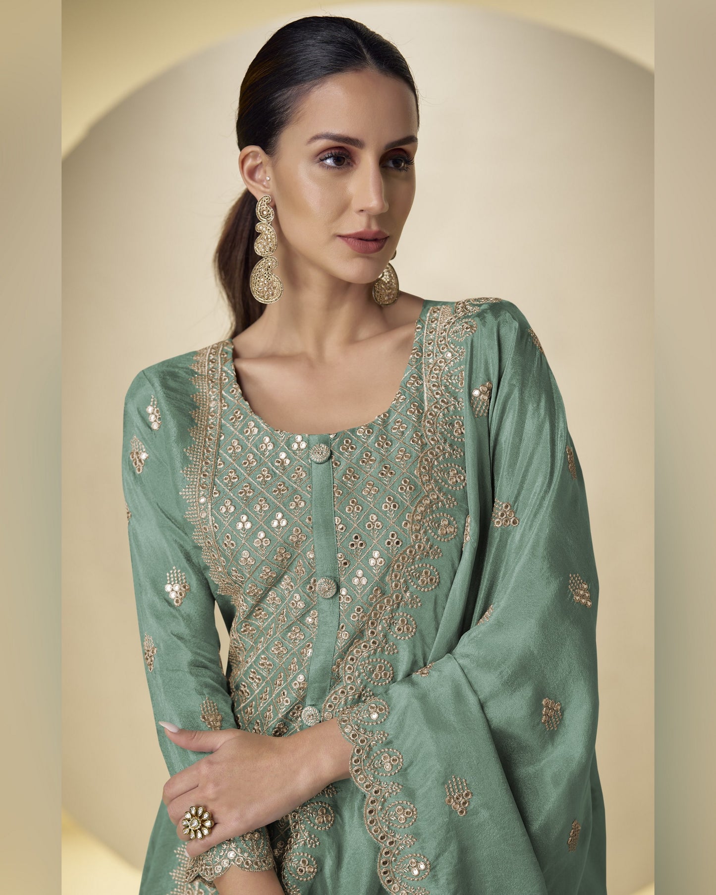 Woman wearing a green embroidered traditional outfit with gold details on a beige background
