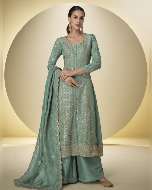 Woman wearing a light green traditional outfit with intricate patterns on a neutral background