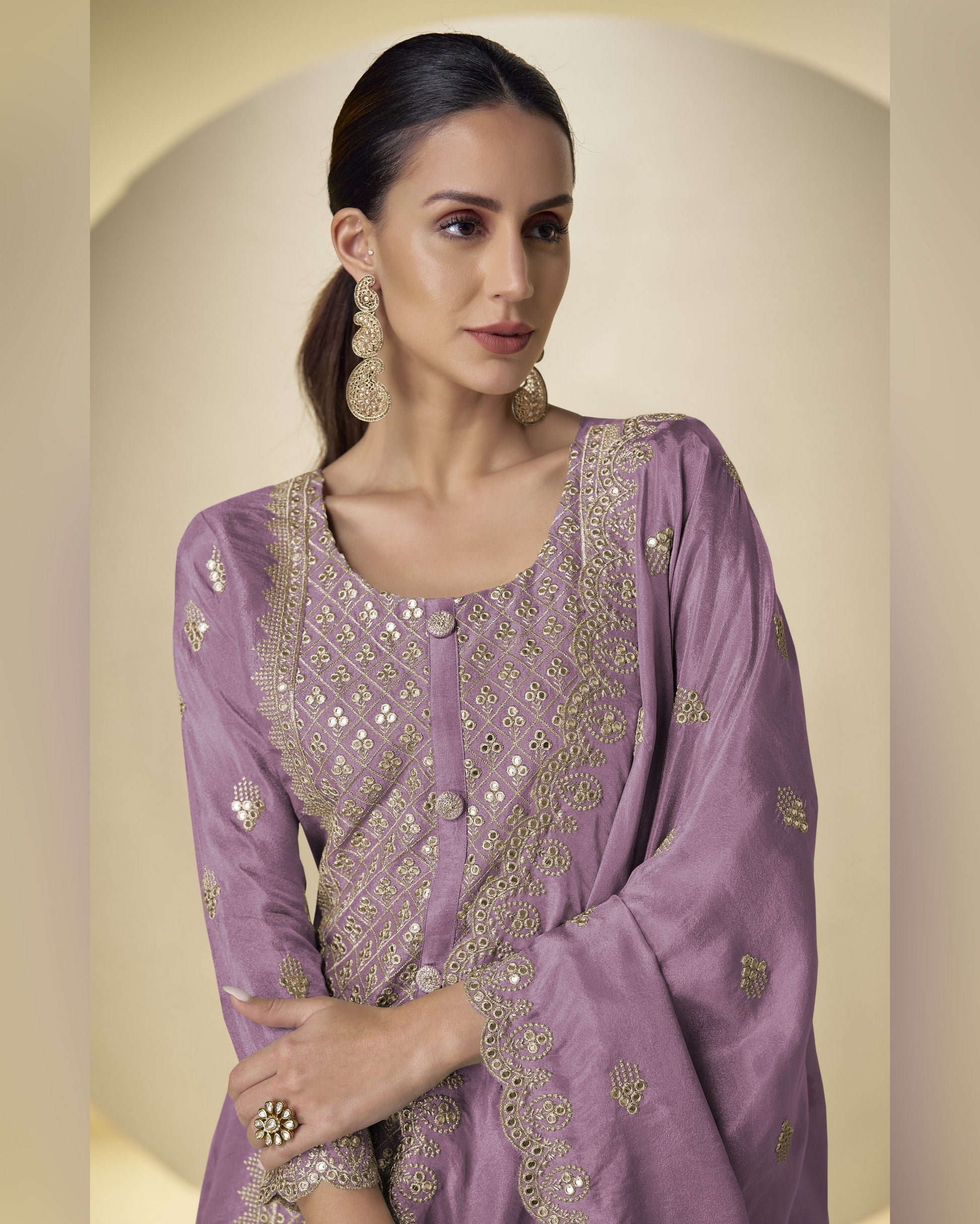 Woman wearing a purple embroidered traditional outfit with gold details on a beige background