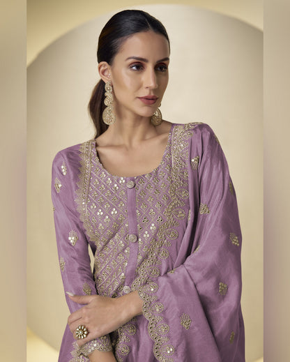 Woman wearing a purple embroidered traditional outfit with gold details on a beige background