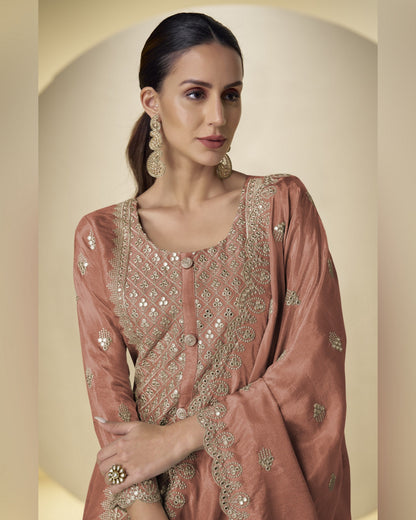 Woman wearing a traditional embroidered pink outfit with gold details against a beige background
