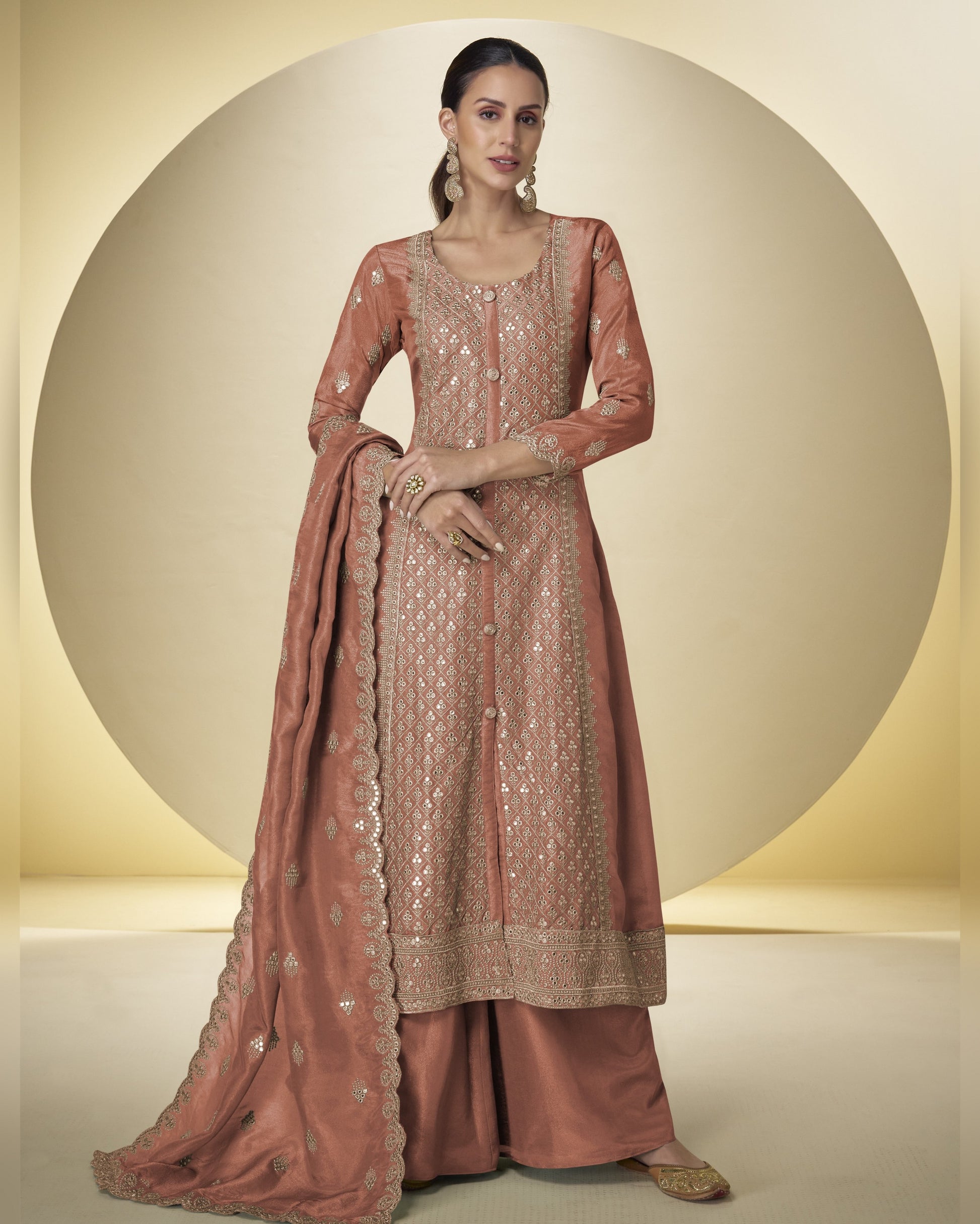 Woman wearing a traditional embroidered pink outfit with a matching dupatta on a beige background