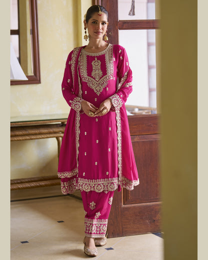 Woman wearing a pink traditional outfit with intricate embroidery in a room.