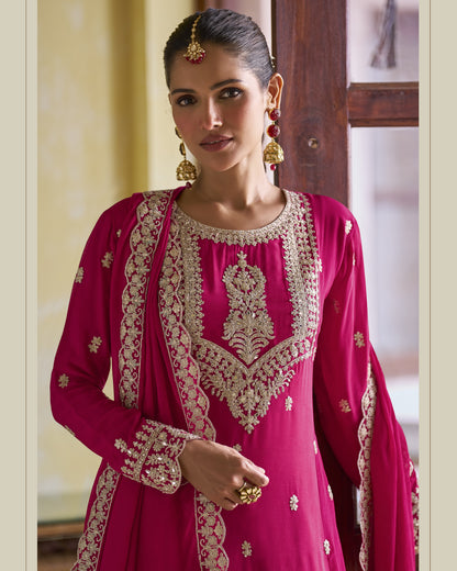 Woman wearing a pink traditional outfit with intricate gold embroidery indoors.