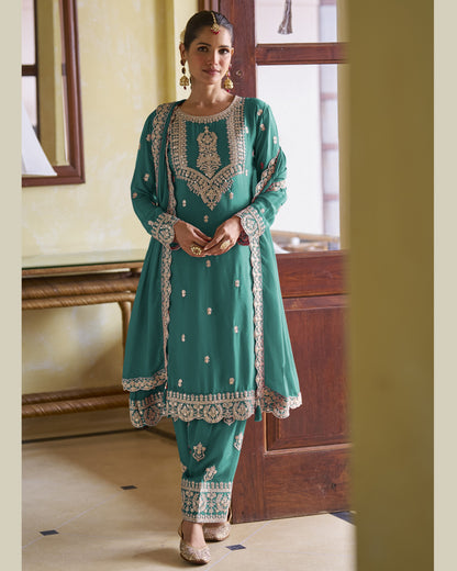 Woman wearing a teal traditional outfit with intricate embroidery in a room.