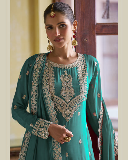 Woman wearing a teal embroidered traditional outfit indoors.
