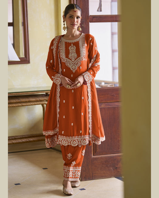 Woman wearing an orange traditional outfit with intricate white embroidery in a room.