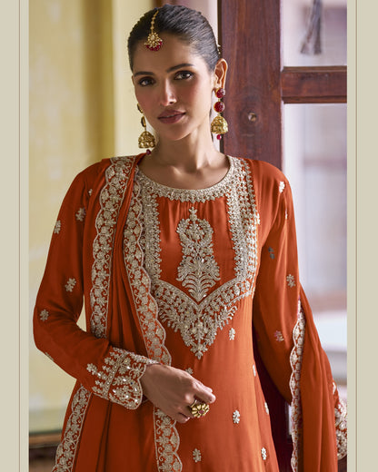 Woman wearing an orange traditional outfit with intricate white embroidery in a room setting.