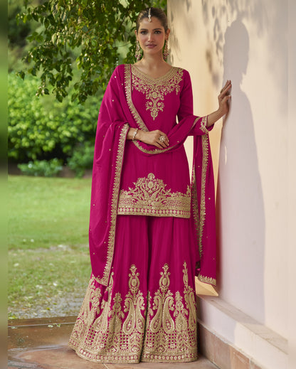 Woman in a pink and gold embroidered traditional outfit standing outdoors.