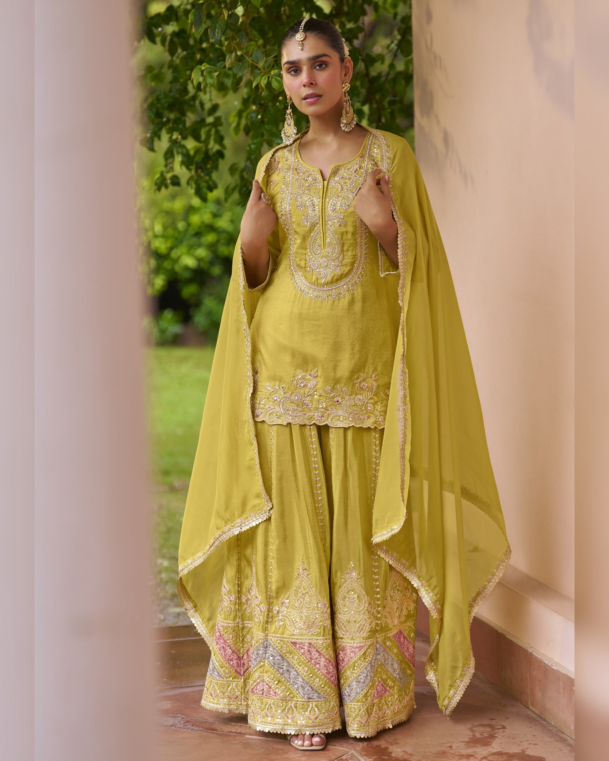 Woman in a yellow embroidered traditional outfit standing outdoors.