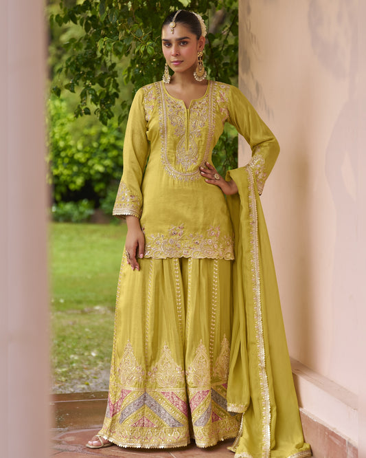 Woman in a traditional green outfit with intricate embroidery standing outdoors.