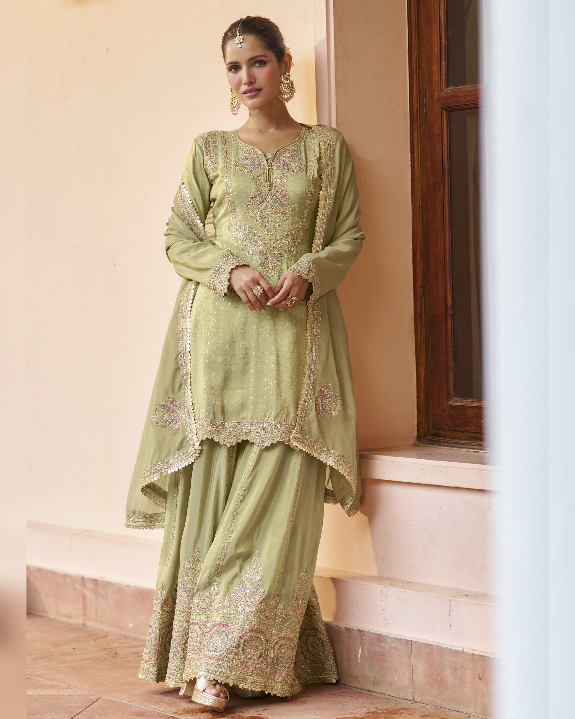 Woman wearing a light green traditional outfit with embroidery, standing indoors.