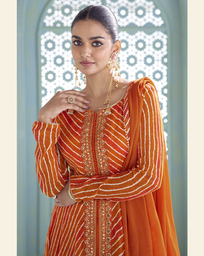 A woman modeling a traditional Indian outfit featuring a bright orange kurta with white stripes and gold embroidery, paired with a matching orange dupatta, set against a decorative archway background.