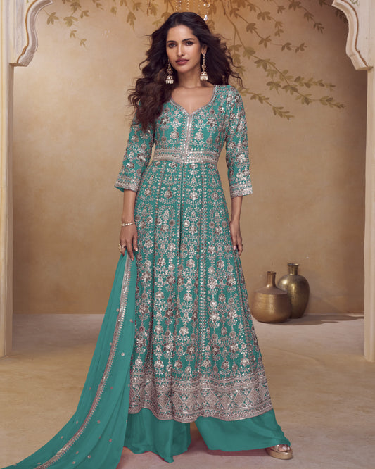 Woman wearing a teal and silver embroidered traditional outfit with a matching dupatta in a decorative setting.
