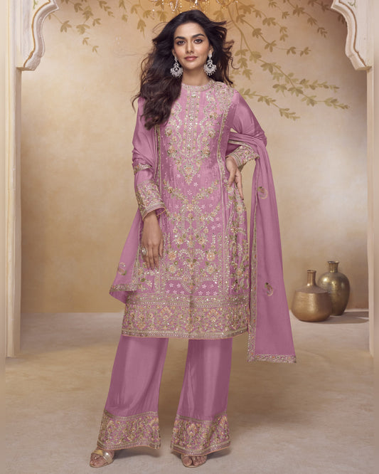 Woman in a traditional pink embroidered outfit with a matching dupatta in a decorated room.