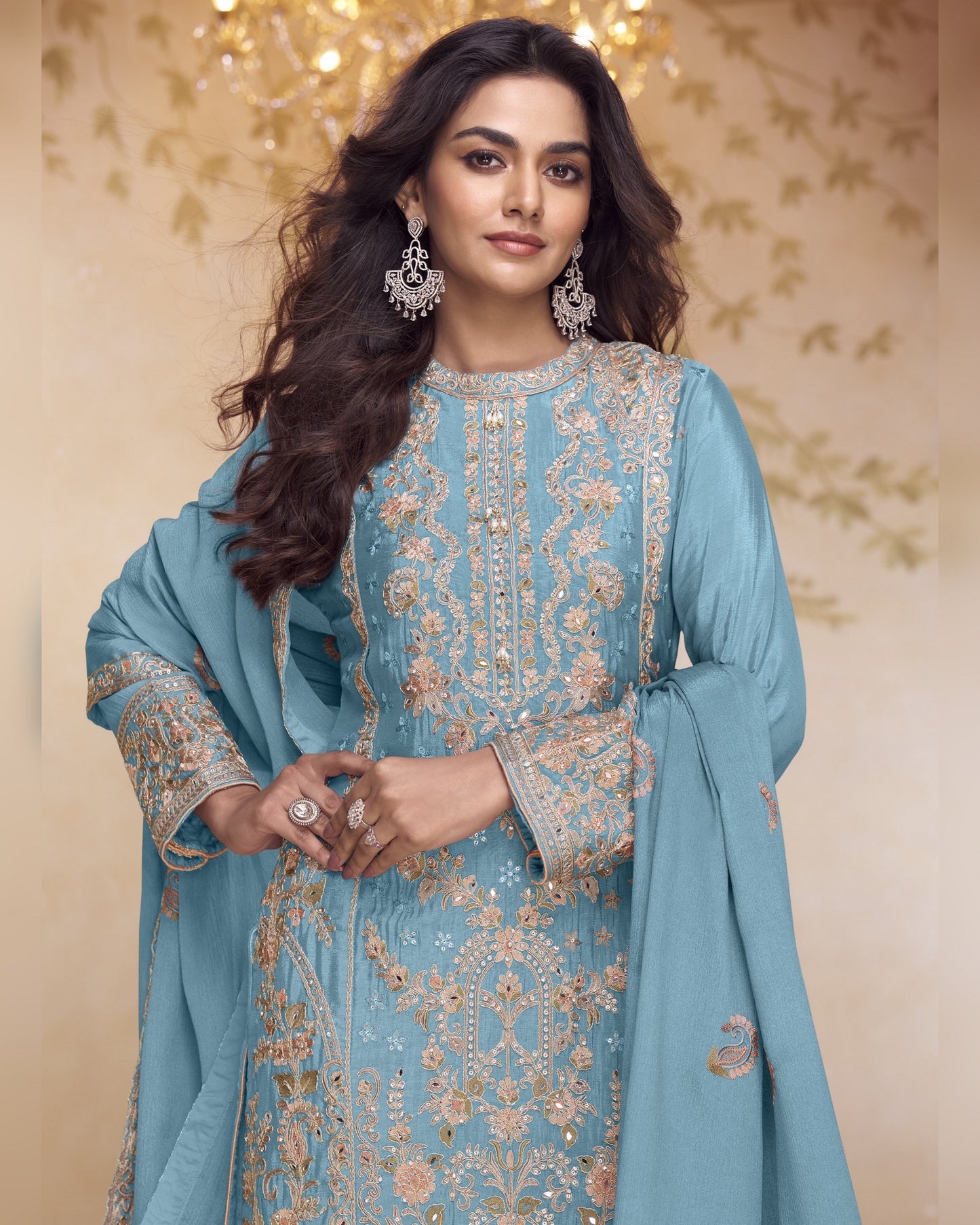 Woman wearing a light blue embroidered traditional outfit with a matching dupatta against a decorative background.
