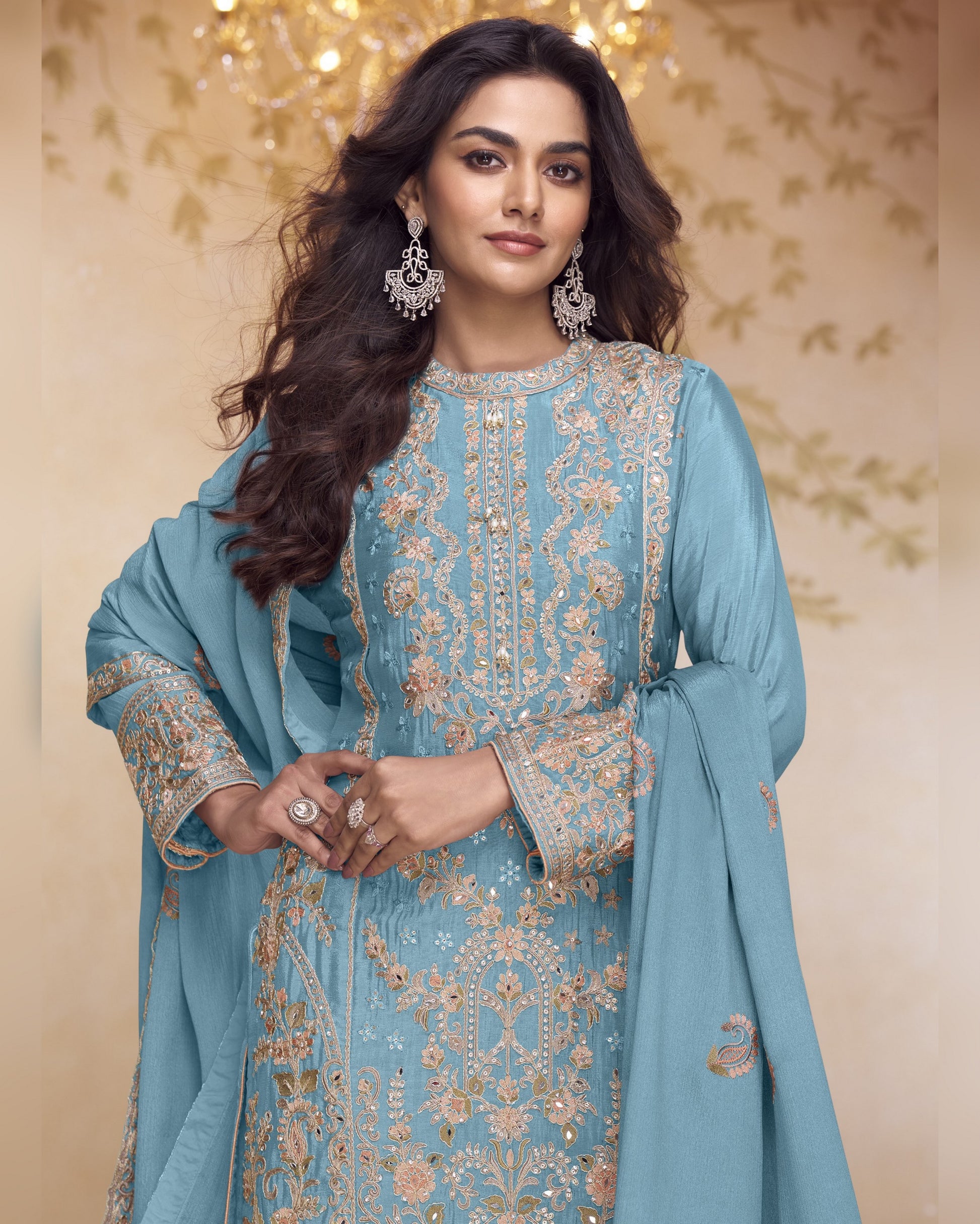 Woman wearing a light blue embroidered traditional outfit with a matching dupatta against a decorative background.