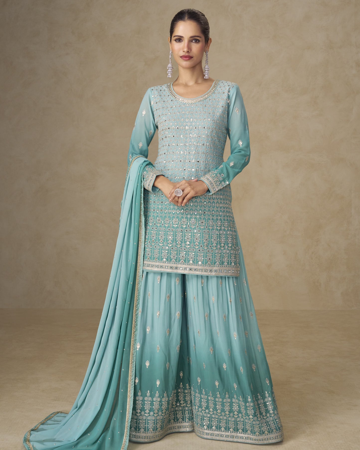 Woman wearing a light blue embroidered traditional outfit with a matching dupatta on a beige background