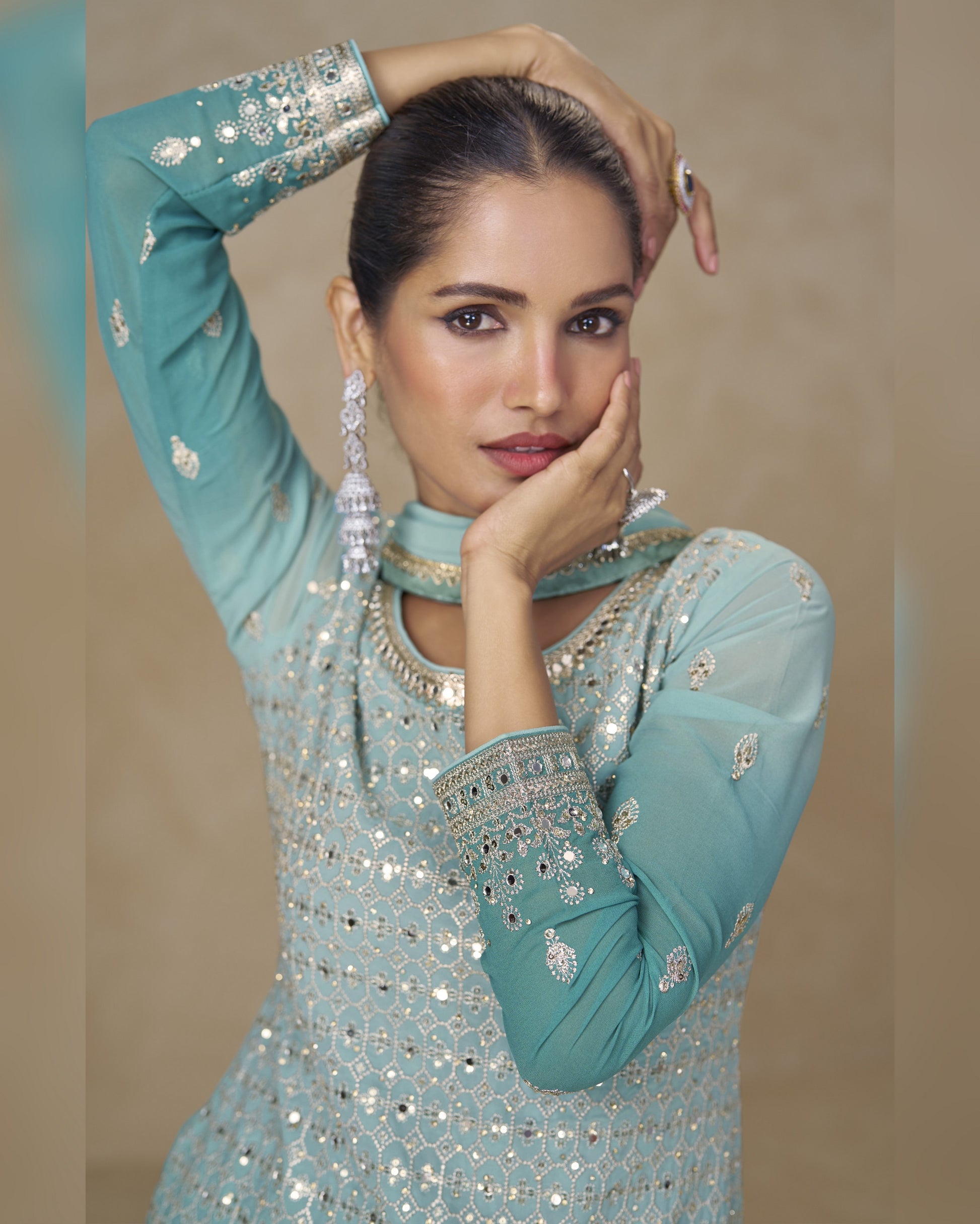 Woman wearing a light blue embroidered traditional outfit against a beige background