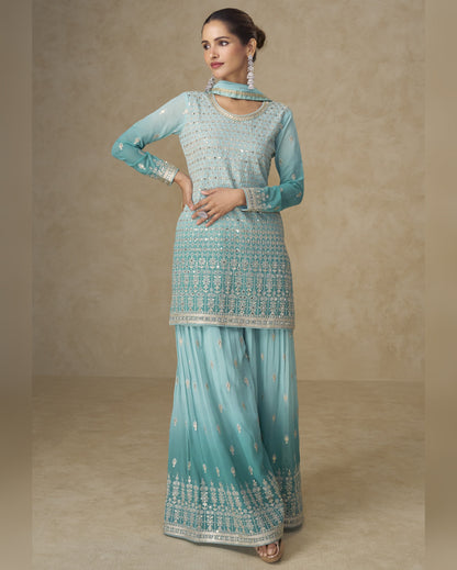 Woman wearing a light blue traditional outfit with intricate patterns on a beige background
