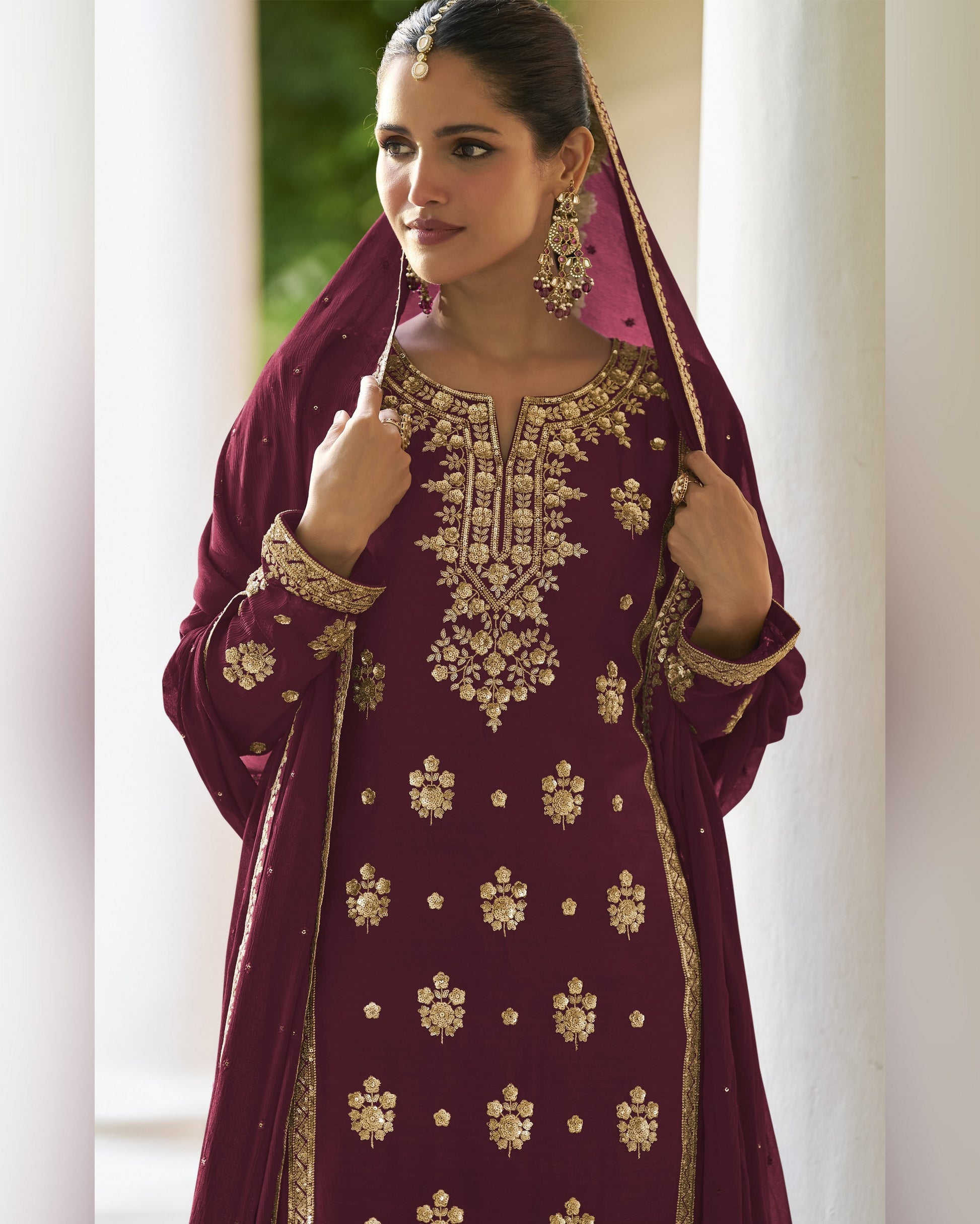 Woman wearing a maroon embroidered traditional outfit with gold details indoors.