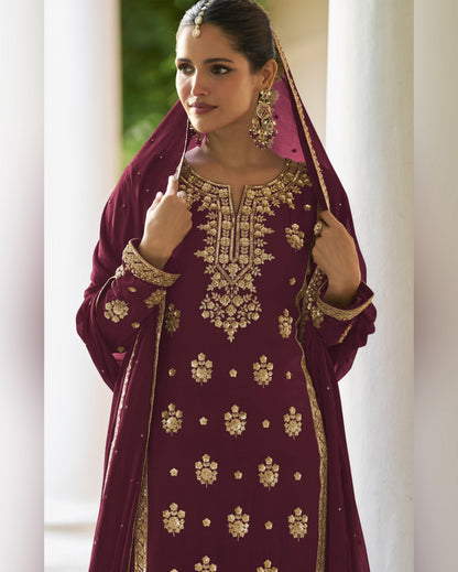 Woman wearing a maroon embroidered traditional outfit with gold details indoors.