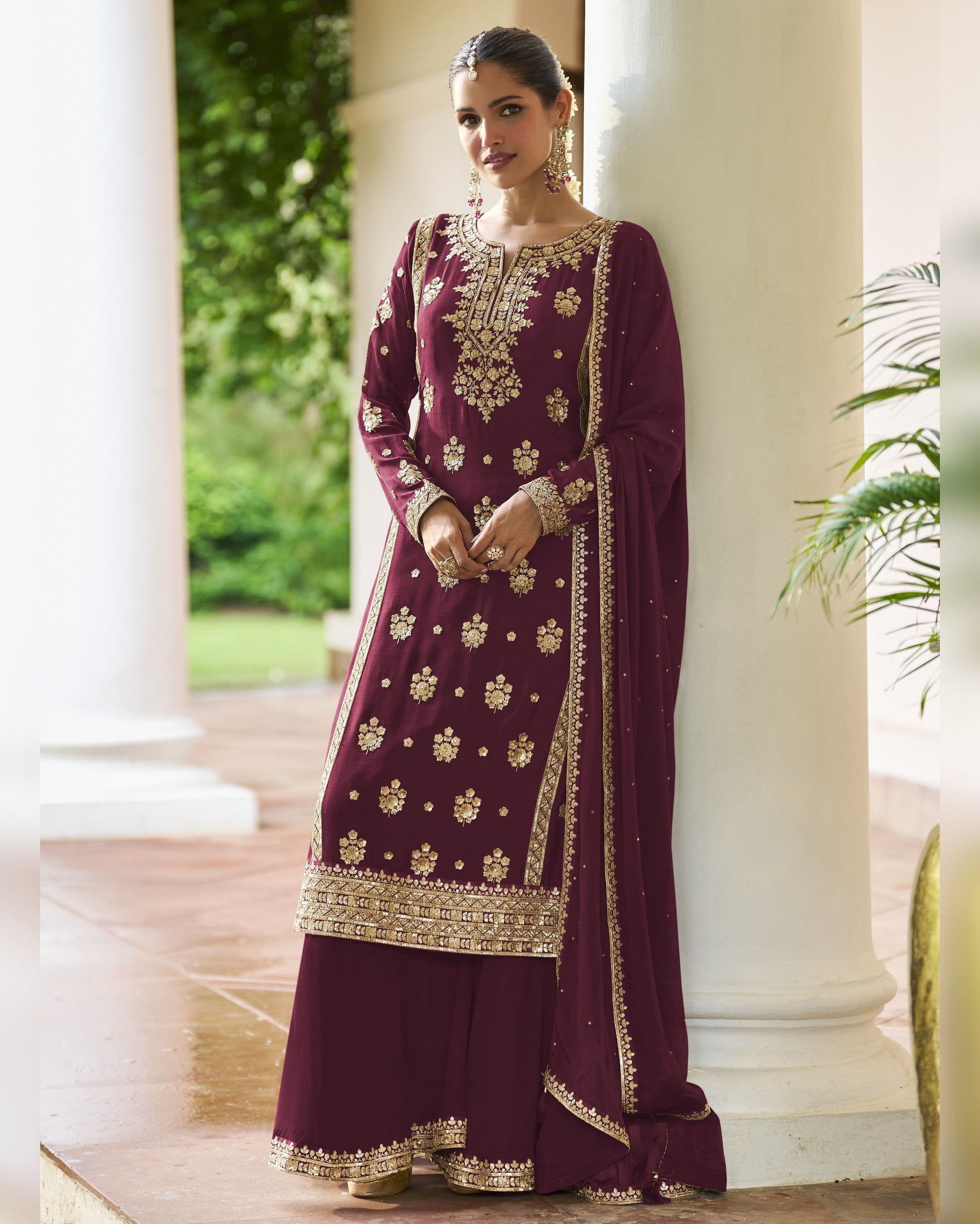 Woman wearing a maroon traditional outfit with gold embroidery in an outdoor setting.