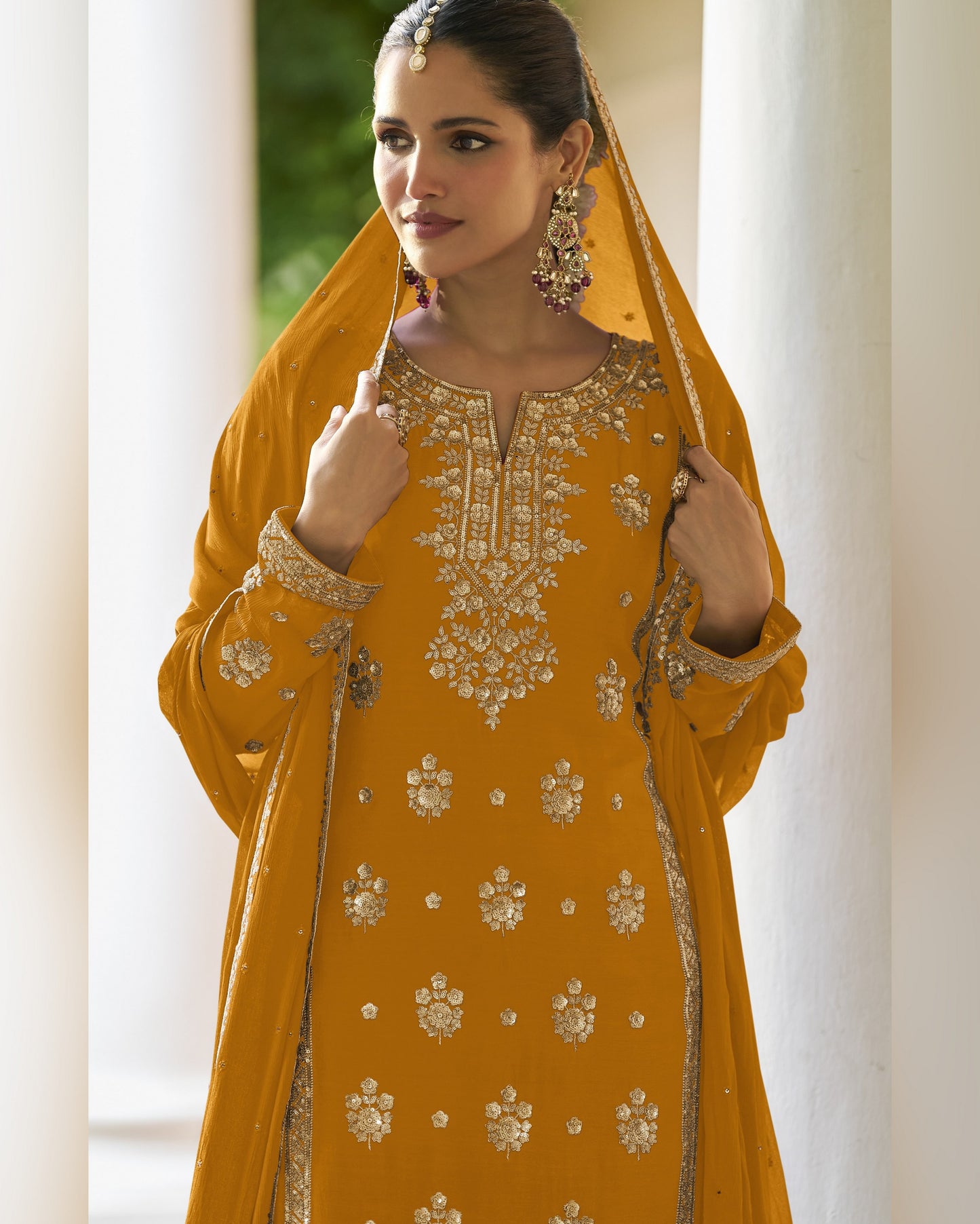 Woman wearing a mustard yellow embroidered traditional outfit with a dupatta.