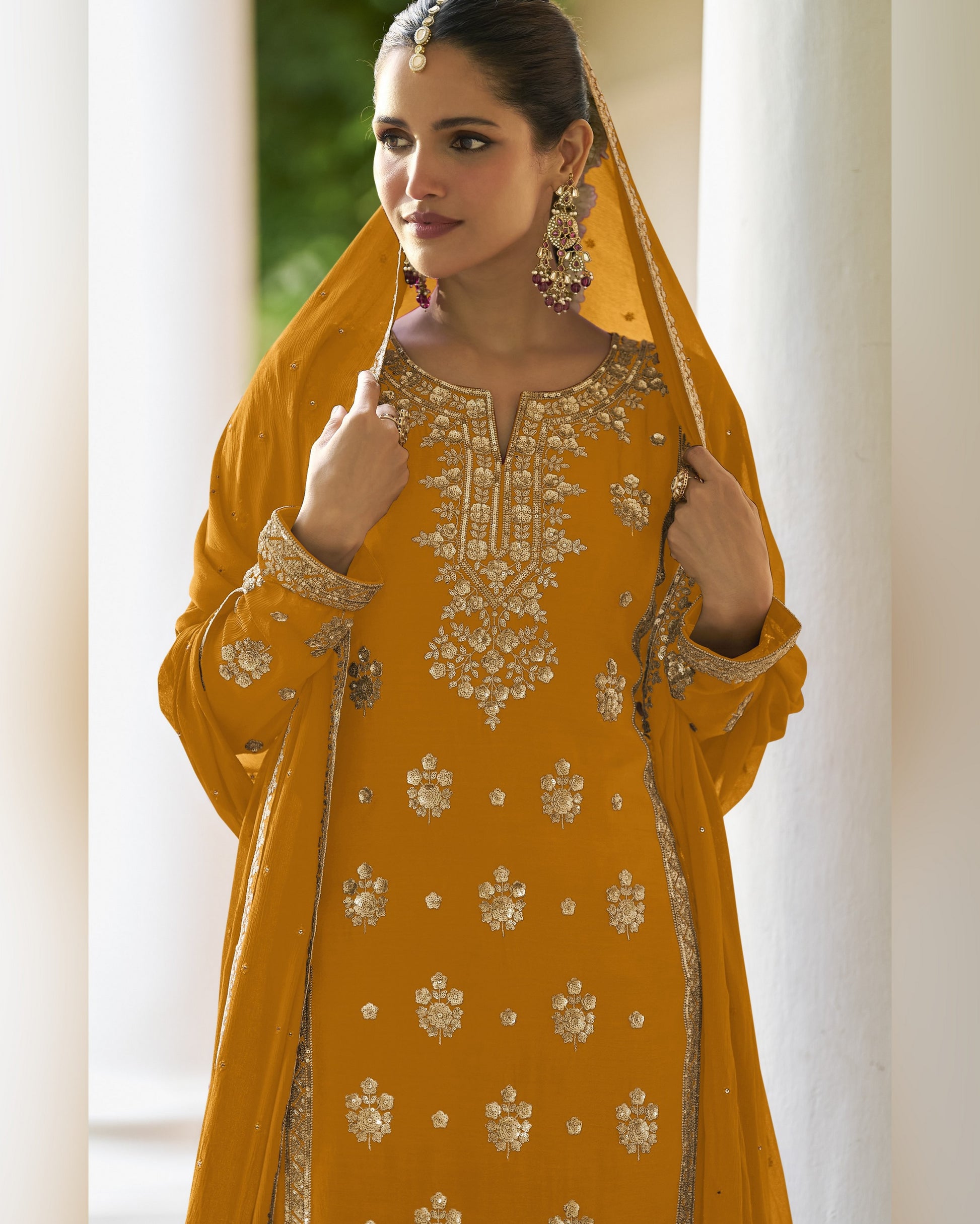 Woman wearing a mustard yellow embroidered traditional outfit with a dupatta.