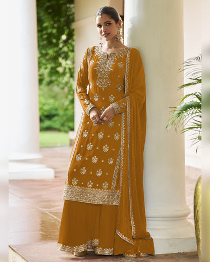 Woman in a mustard yellow traditional outfit with intricate patterns standing outdoors.