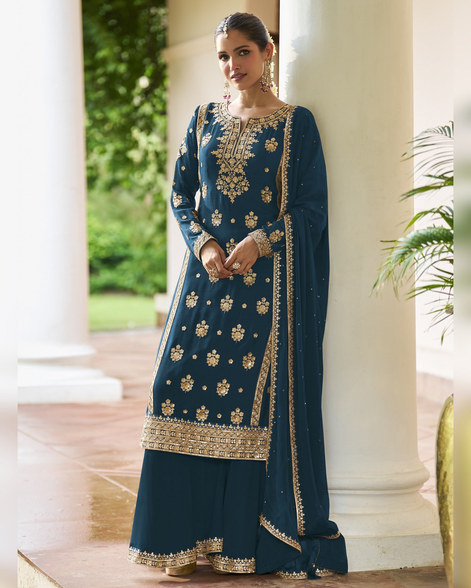 Woman in a blue embroidered traditional outfit standing outdoors.
