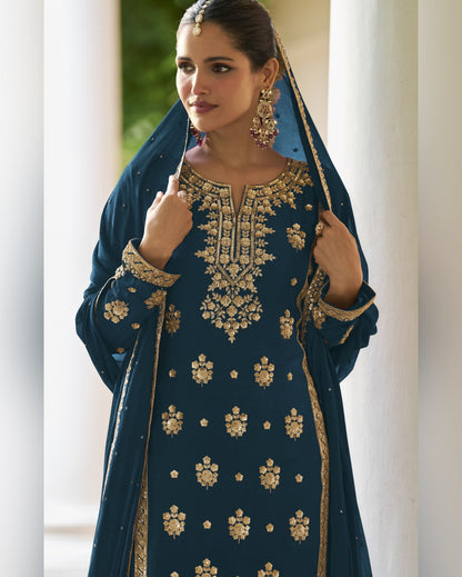 Woman wearing a blue embroidered traditional outfit with gold details.