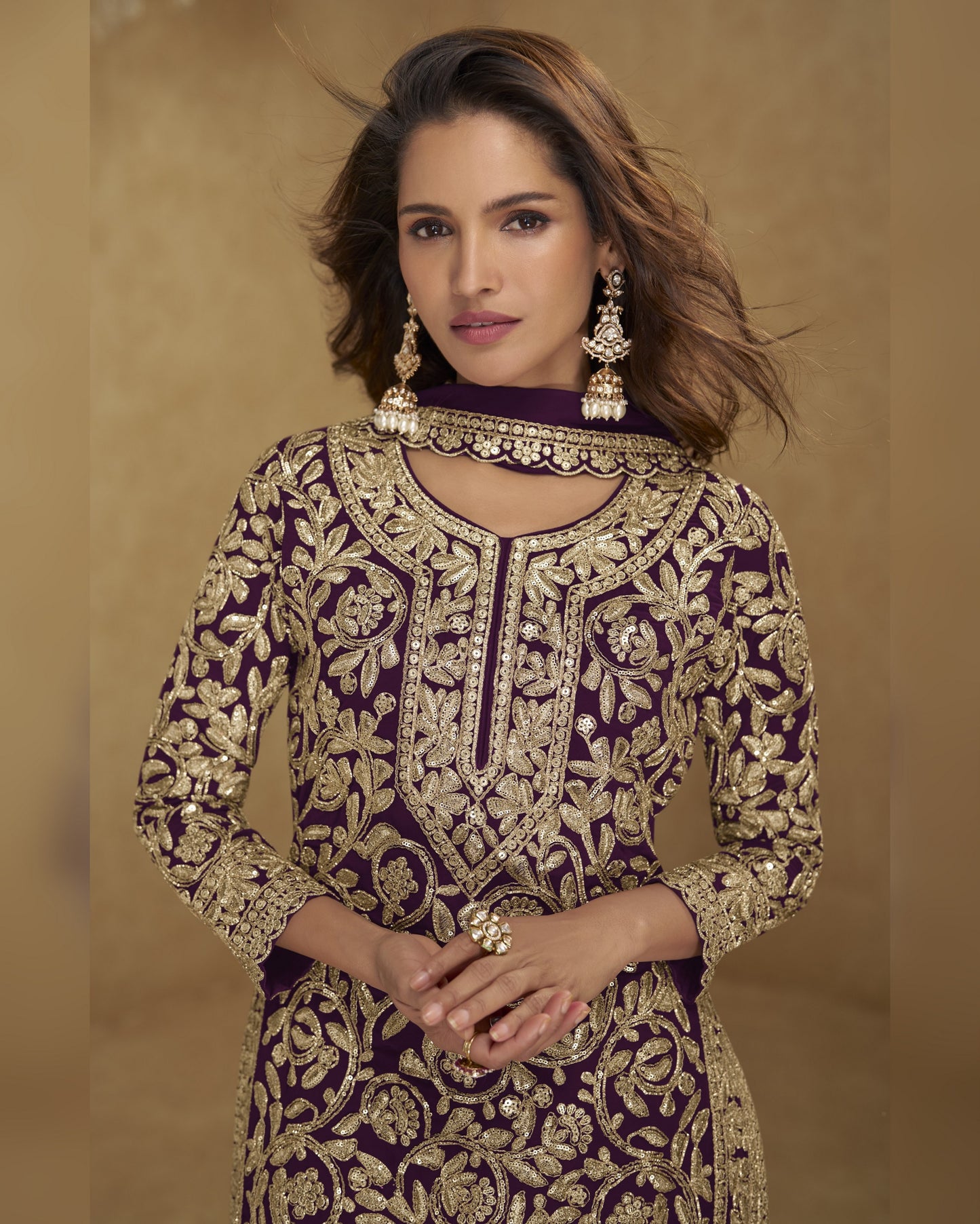 Woman wearing a purple and gold embroidered traditional outfit with jewelry against a beige background
