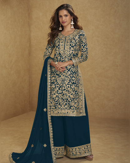 Woman wearing a traditional embroidered outfit with a blue dupatta against a beige background