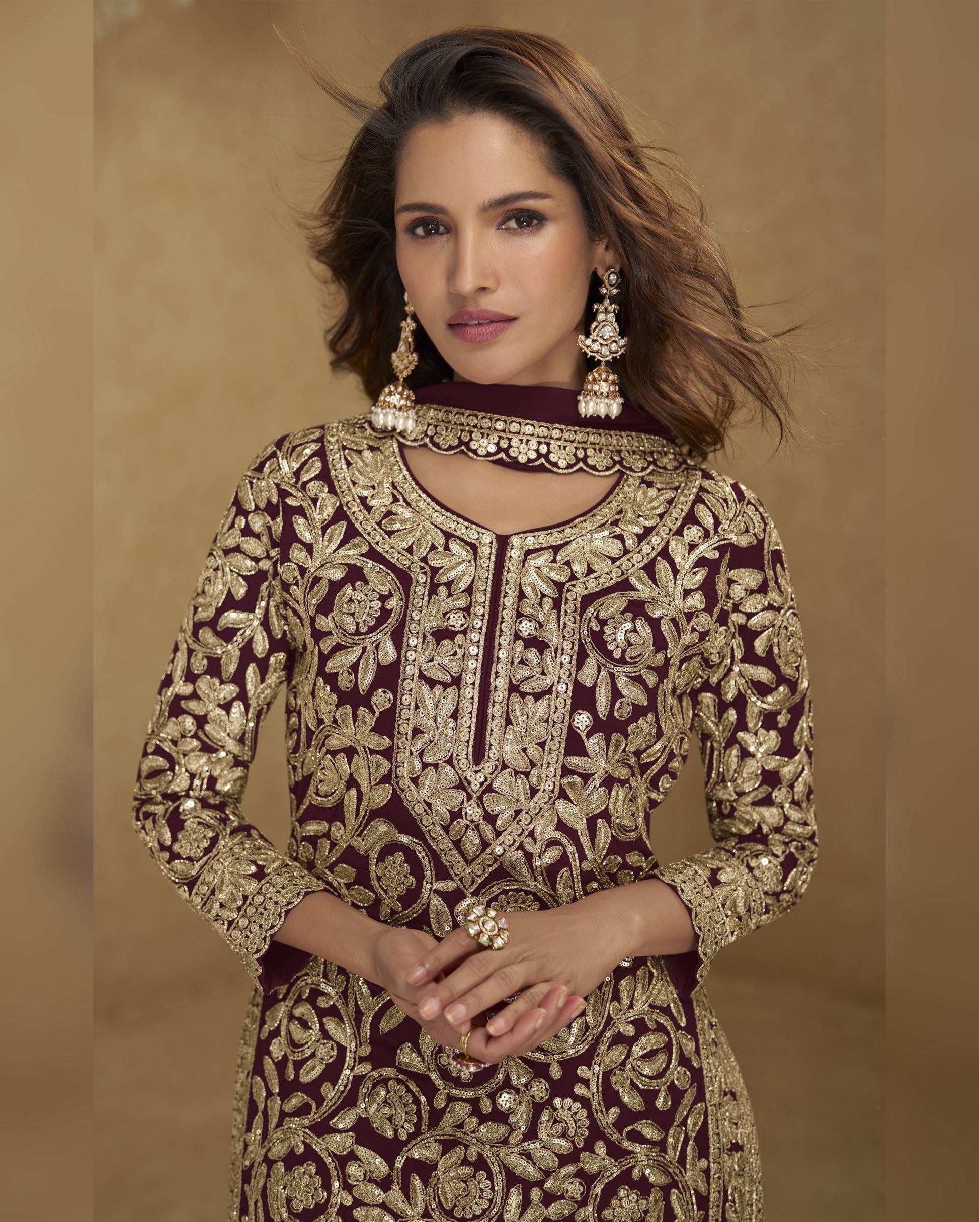 Woman wearing a maroon and gold embroidered traditional outfit against a beige background