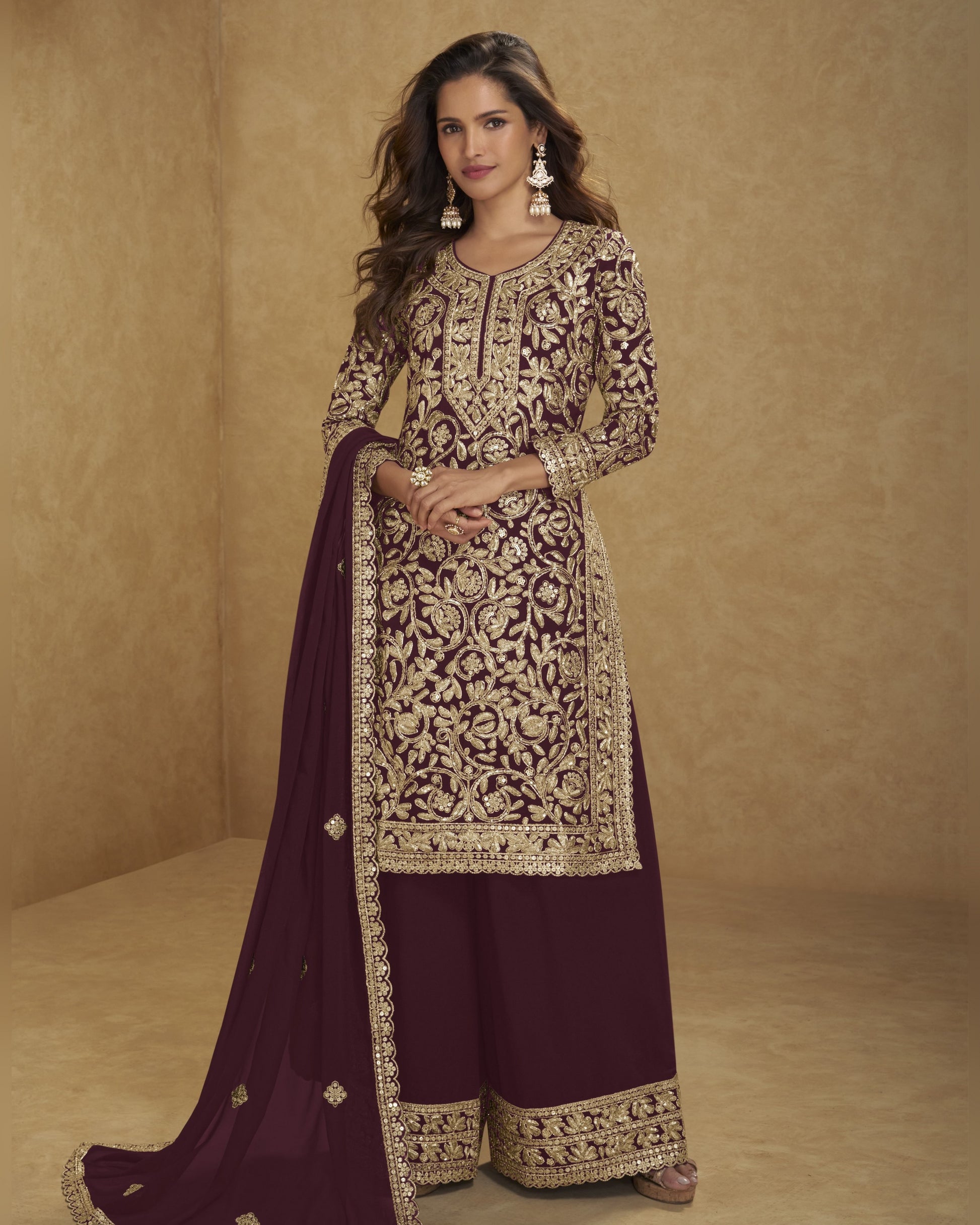 Woman wearing a traditional embroidered outfit with a maroon dupatta against a beige background